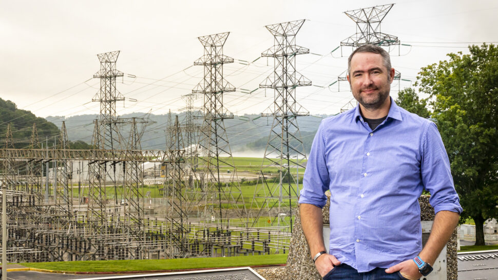 Man standing in a field with large power lines in the background