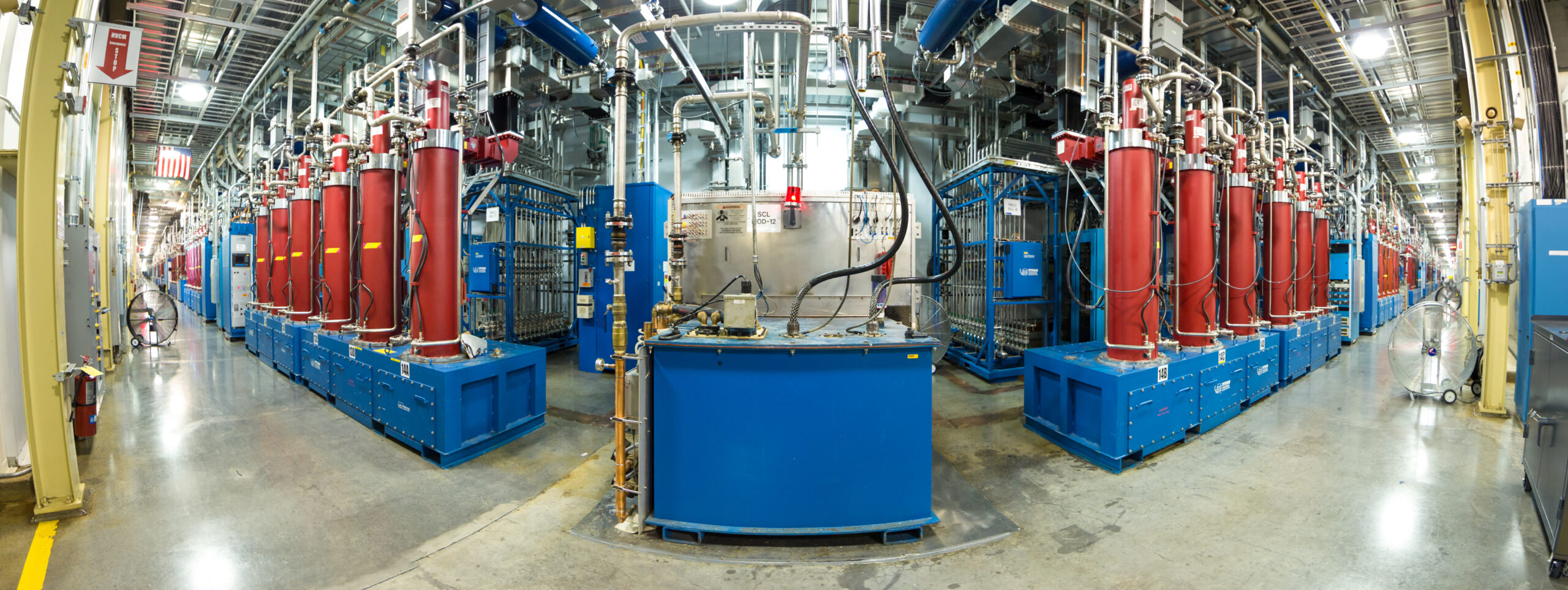 Industrial facility with rows of red tanks, blue machinery, and overhead piping.