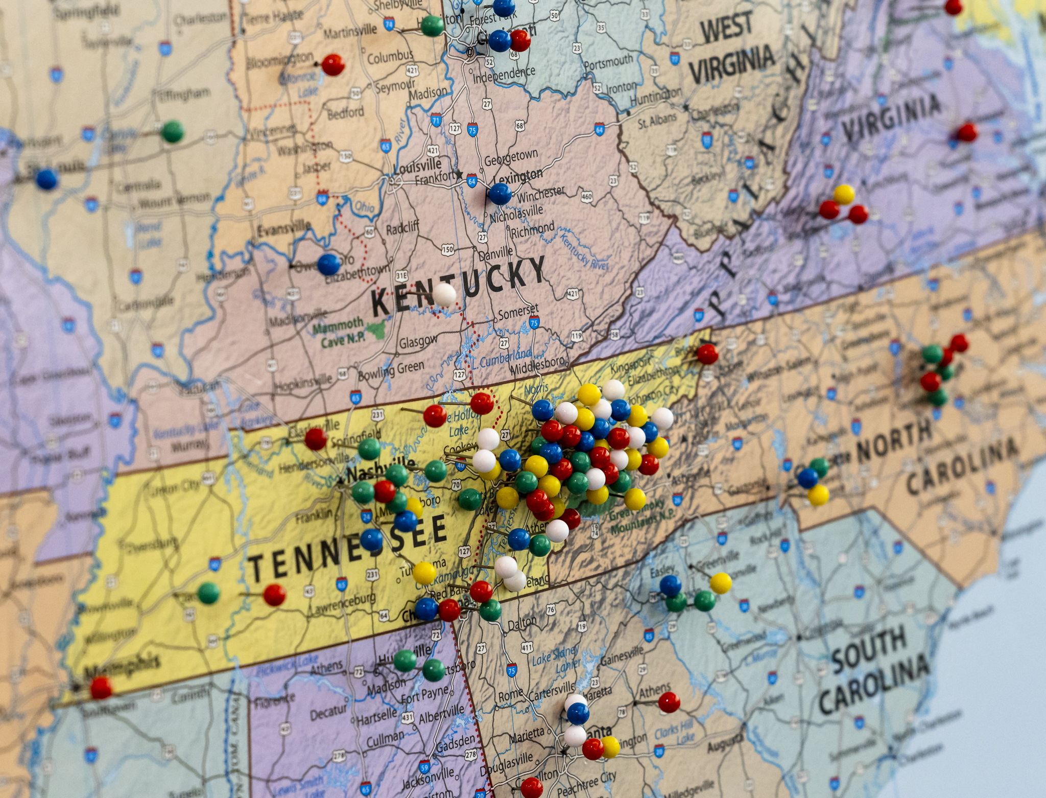 Close-up of a wall map of the southeastern United States covered with multicolored pushpins marking locations across Tennessee, Kentucky, North Carolina, South Carolina, Virginia, and neighboring states. A dense cluster of pins is concentrated in eastern Tennessee around the Oak Ridge and Knoxville area, with additional markers scattered throughout the surrounding region.