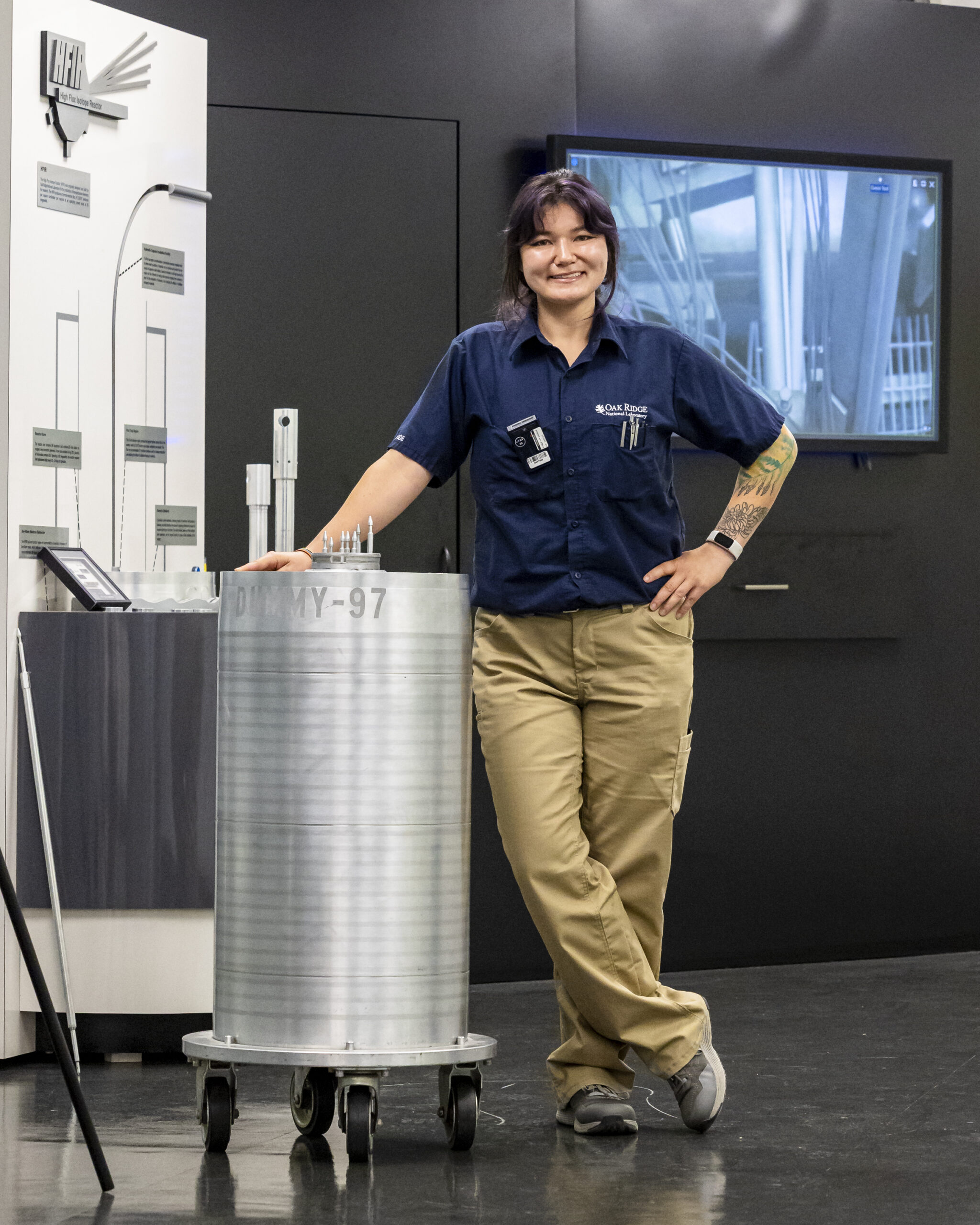 A person standing beside a large cylindrical research device in a laboratory exhibit space.