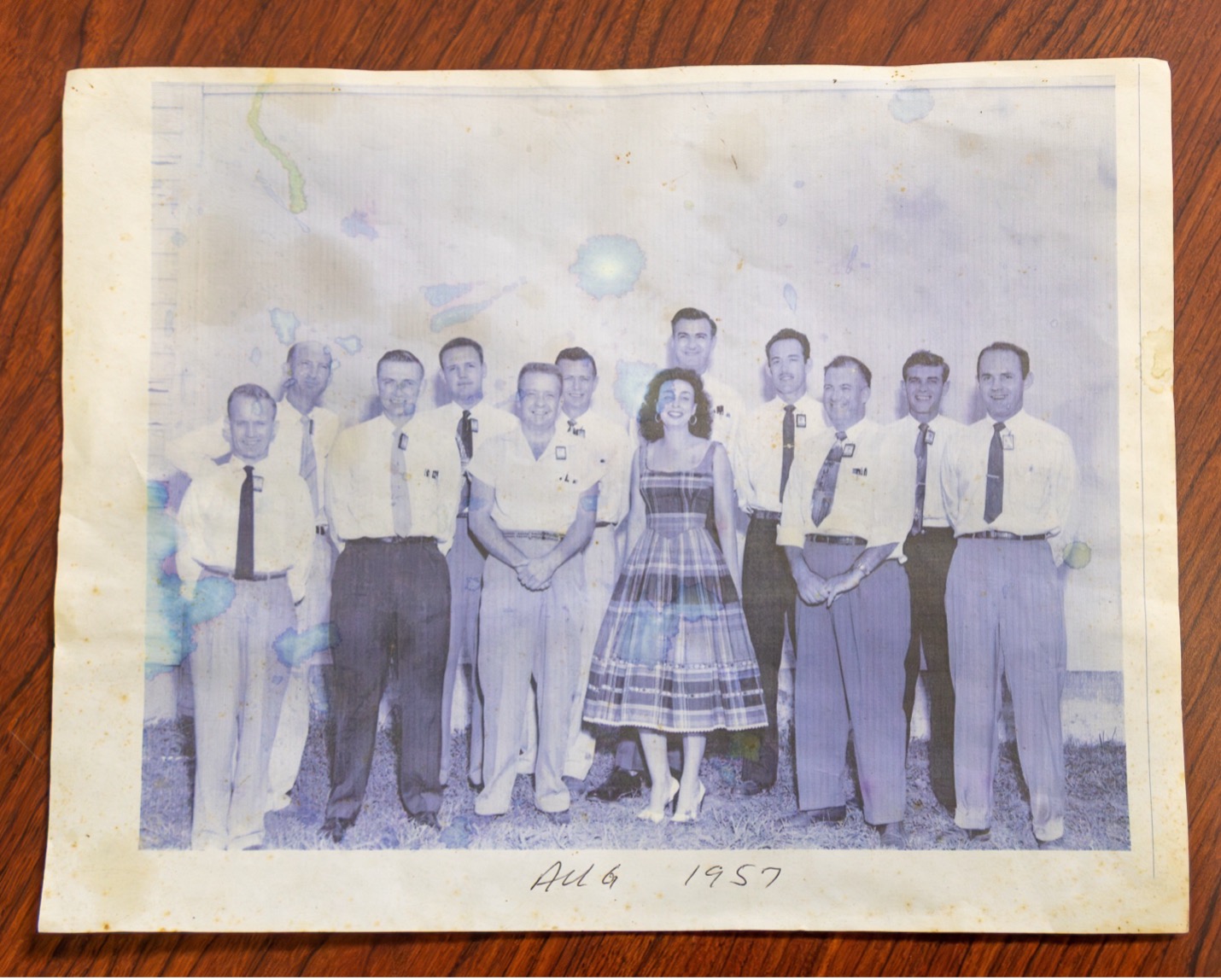 A vintage 1957 group photo of laboratory staff, including one woman, standing outdoors.