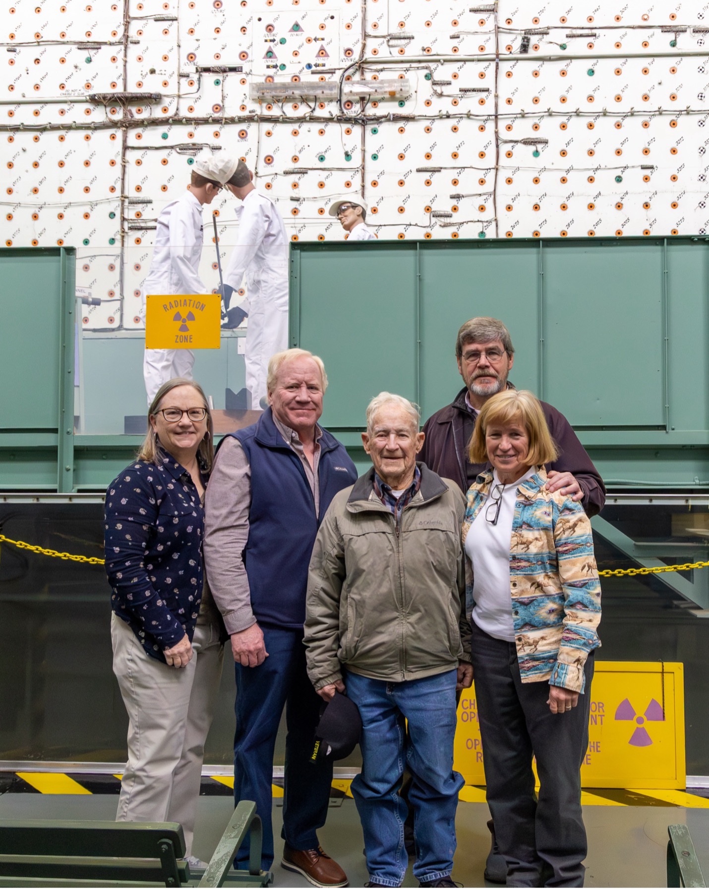 An older man stands with family members in front of a nuclear reactor exhibit at ORNL.
