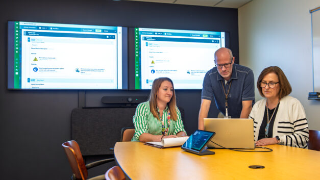 Steve Cline, Tonia Mehlhorn, and Megan Patel collaborate in a meeting room at Oak Ridge National Laboratory while reviewing safety activity plans on a screen.