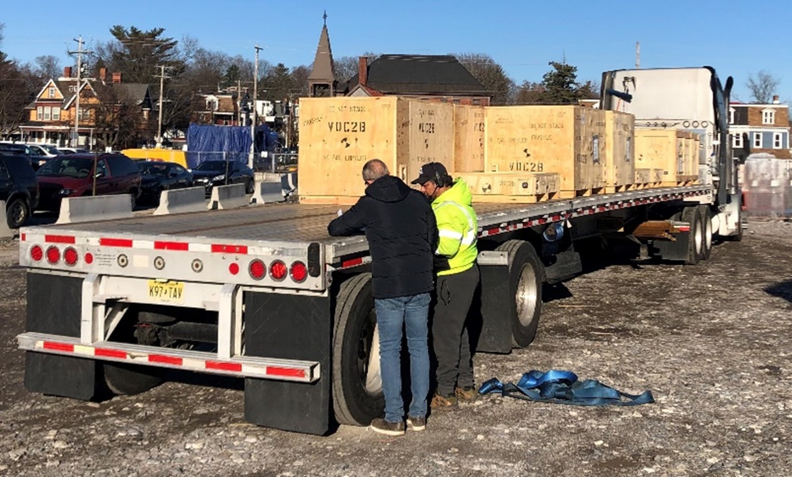 Two men are talking on the backside of a semi trailer holding big wooden boxes