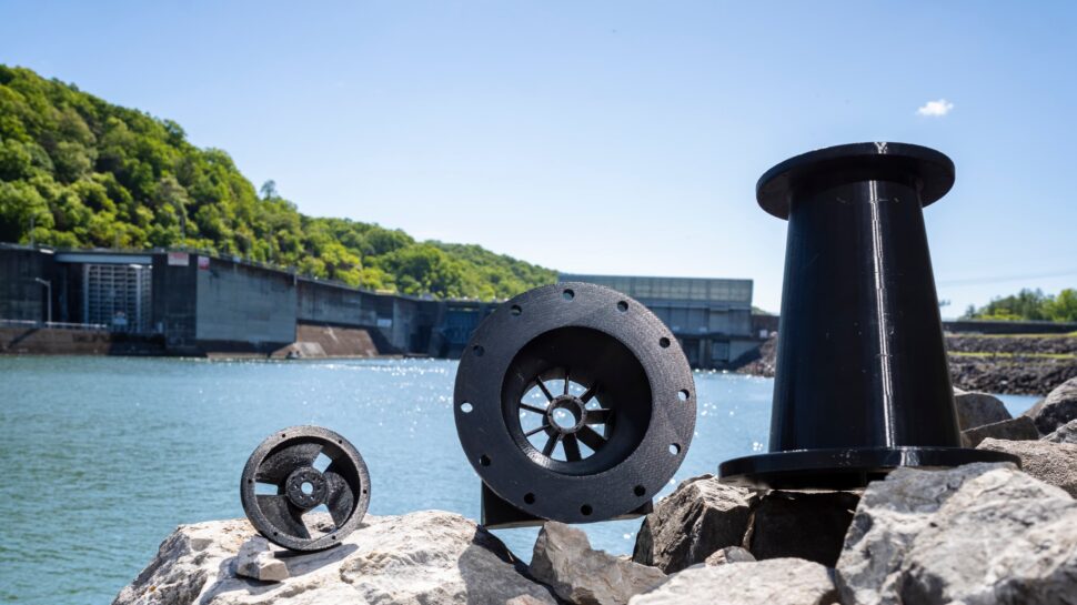 Several parts of water power research are placed on rocks along the bank of the Clinch River. The dam is out of focus in the background, behind the parts.