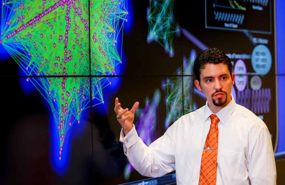 A researcher stands in front of a screen utilizing computational research to drive buildings science.