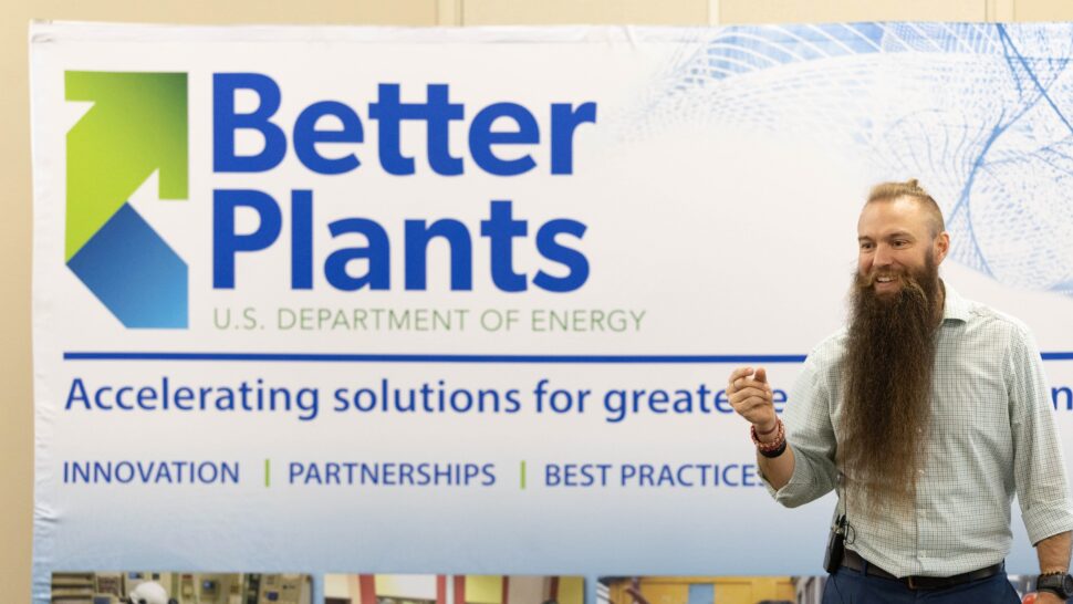 A person with a long beard smiles in front of a sign that reads "Better Plants. U.S. Department of Energy."