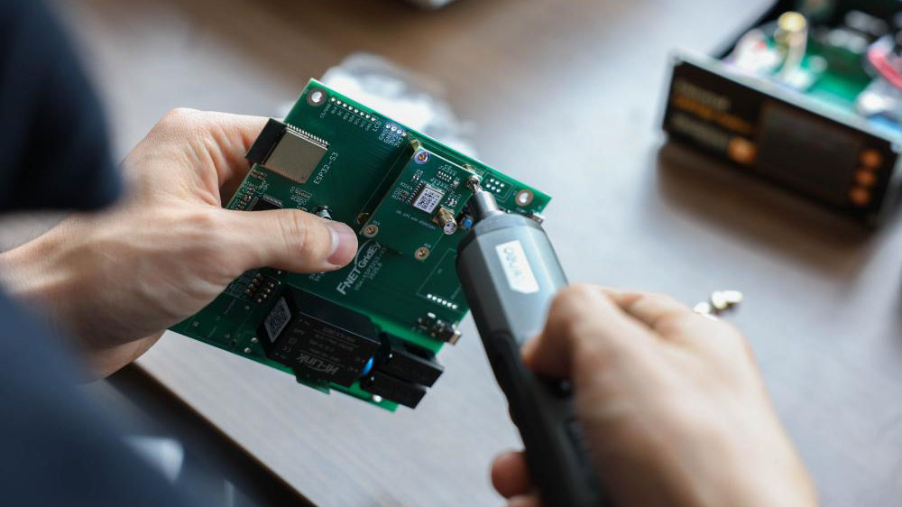 An engineer is utilizing a precision tool on a circuit board to develop the GridEdge Analyzer.