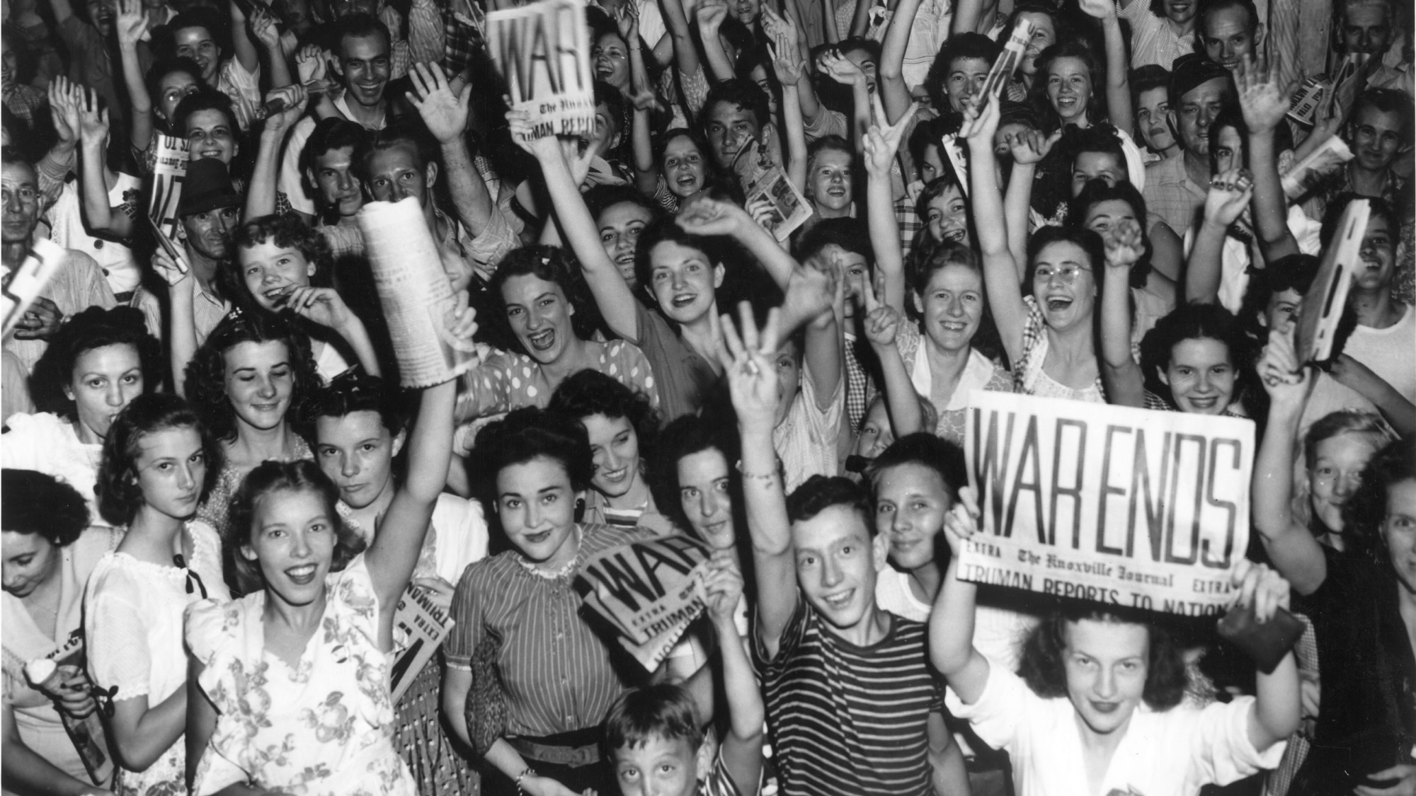 Historic image of Oak Ridge's Jackson Square full of people holding the front page of the news paper that reads "War Ends"