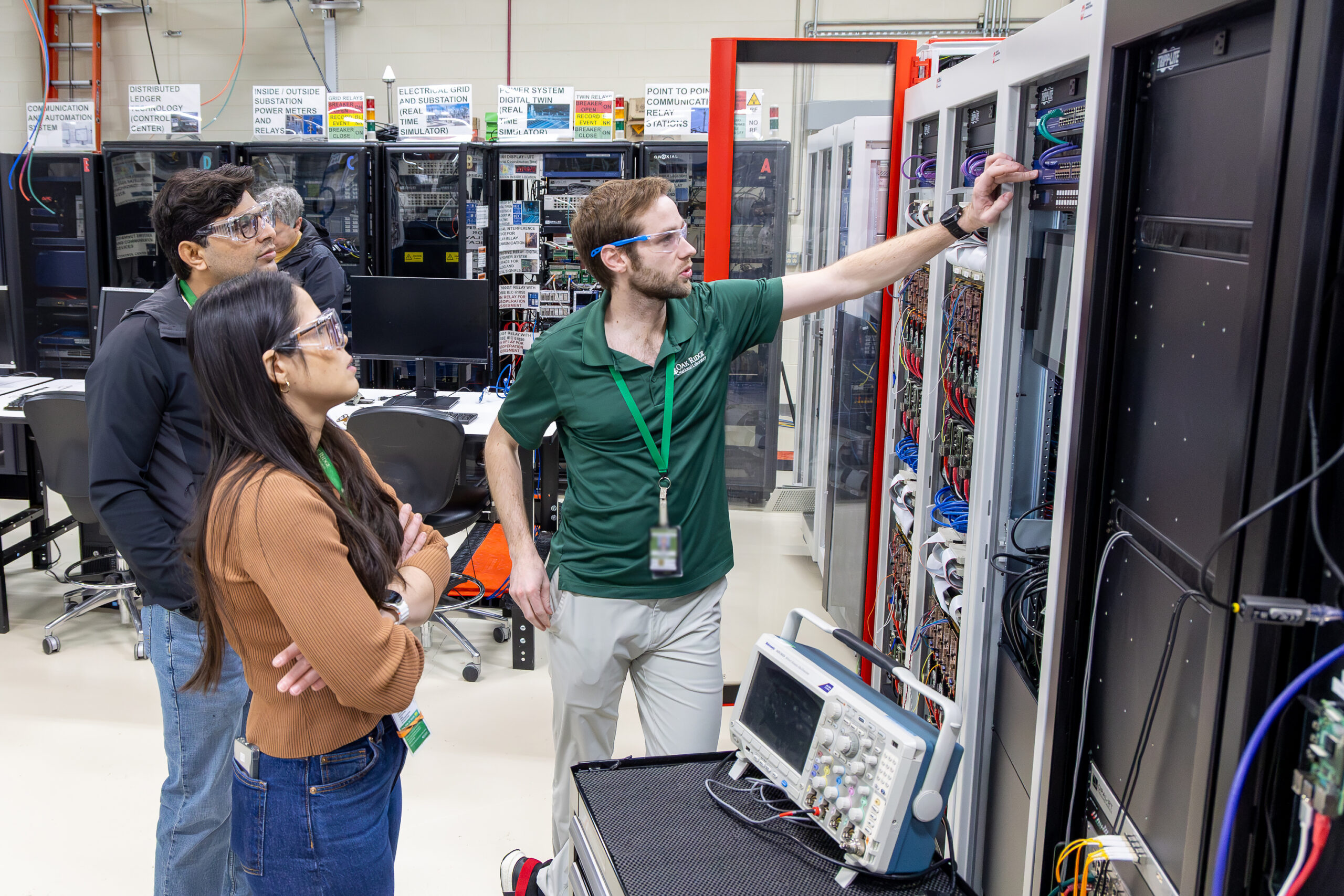 Renata Rezende da Costa Reis Kimpara, Ben Dean and Mohammad Khalid review equipment inside a control rack while discussing lab layout changes in the Grid-C Advanced Protection Lab at Oak Ridge National Laboratory.