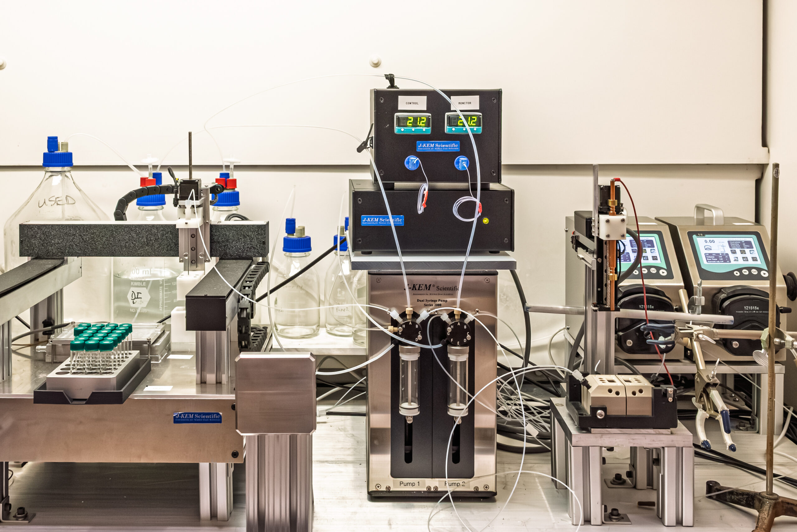 Automated laboratory instrument with pumps, tubing, and sample vials on a bench.