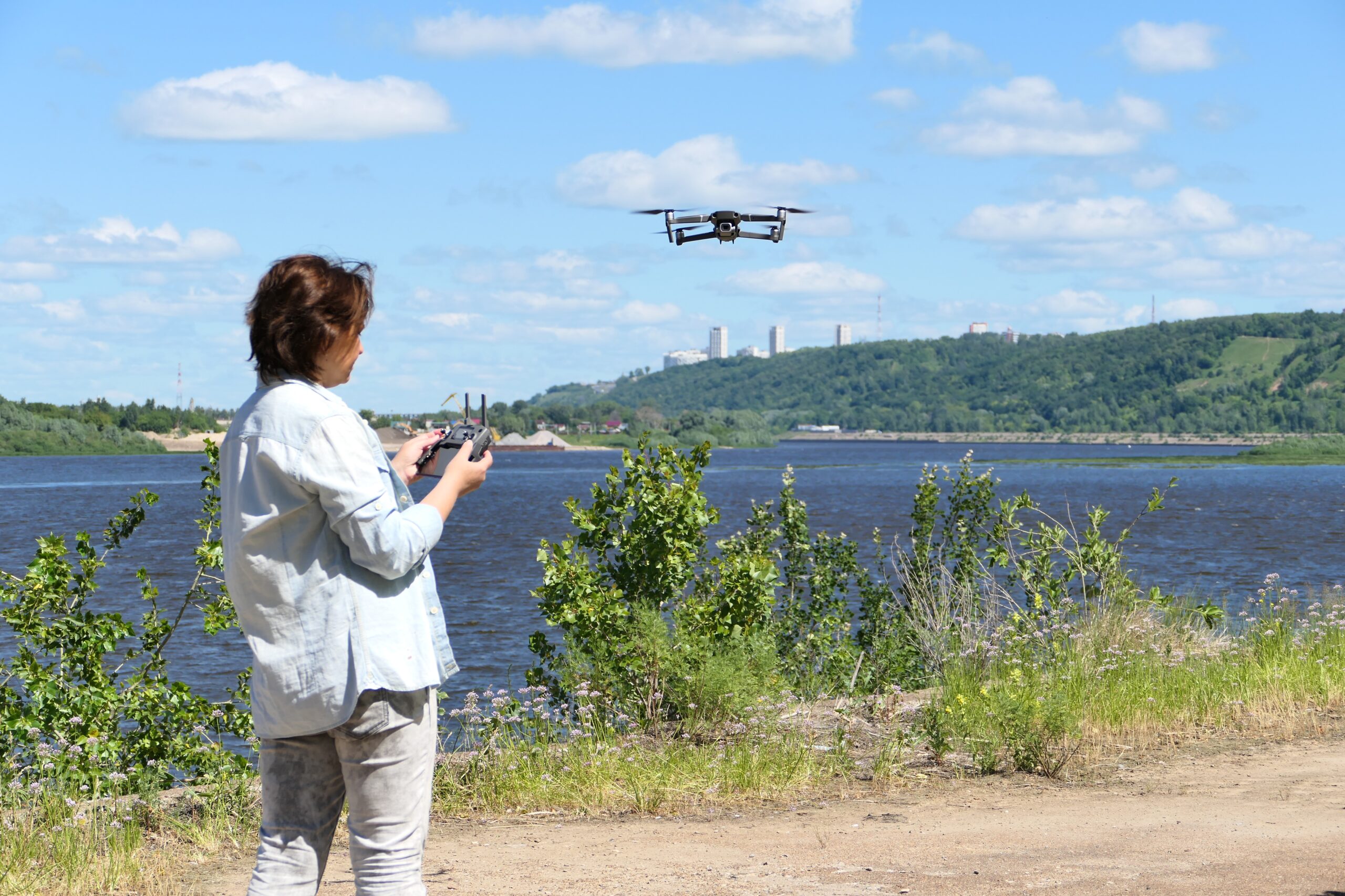 A woman operates a drone near a lake