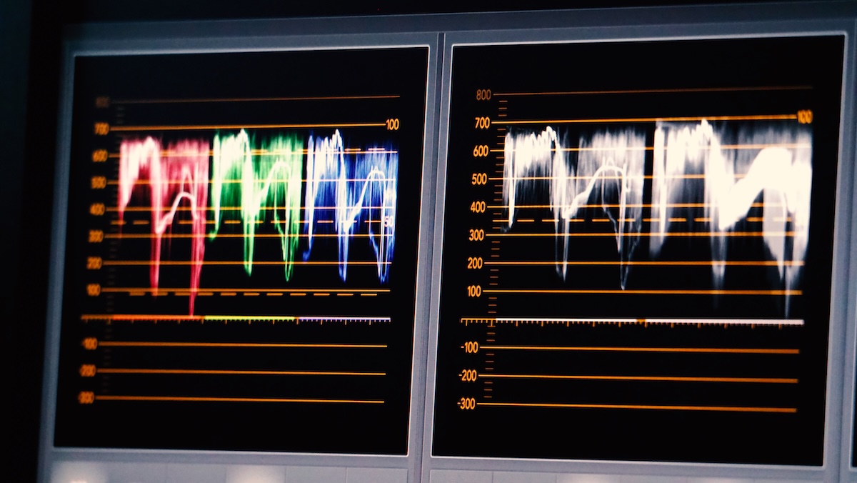 A computer monitor displays a wave form, showing vivid and intense data. The red, green and blue colored lines are shown on a black background with orange horizontal lines. Image from Envato