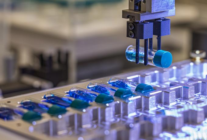 A robotic arm in a laboratory clasps a test tube filled with blue liquid.