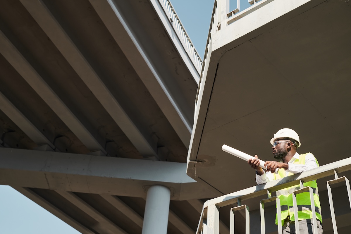 Construction engineers wearing safety vests and work helmets standing at construction site and working on apartment building project. Image from Envato