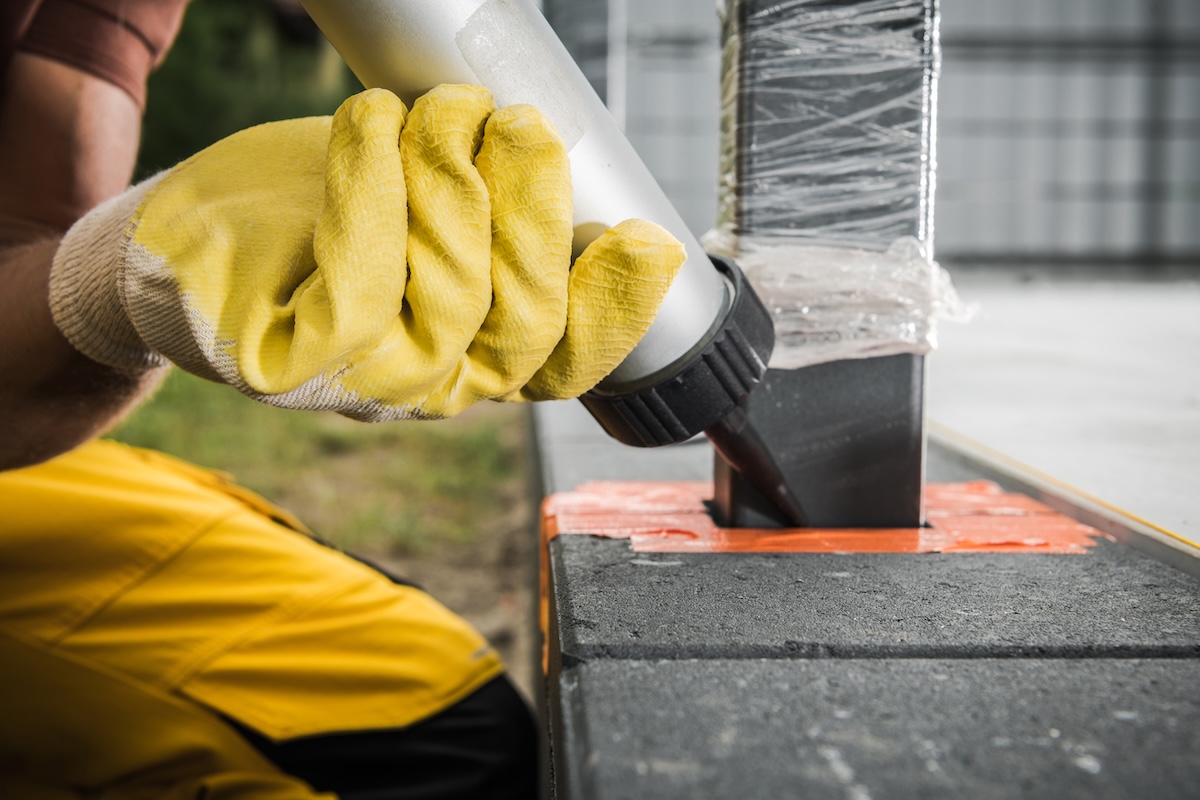 Worker injects silicone material between fence pole and concrete bricks. Image from Envato.