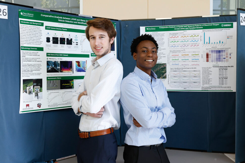 Summer interns stand beside research posters and discuss their projects with attendees during the Summer Student Poster Session in Building 5700 at ORNL.