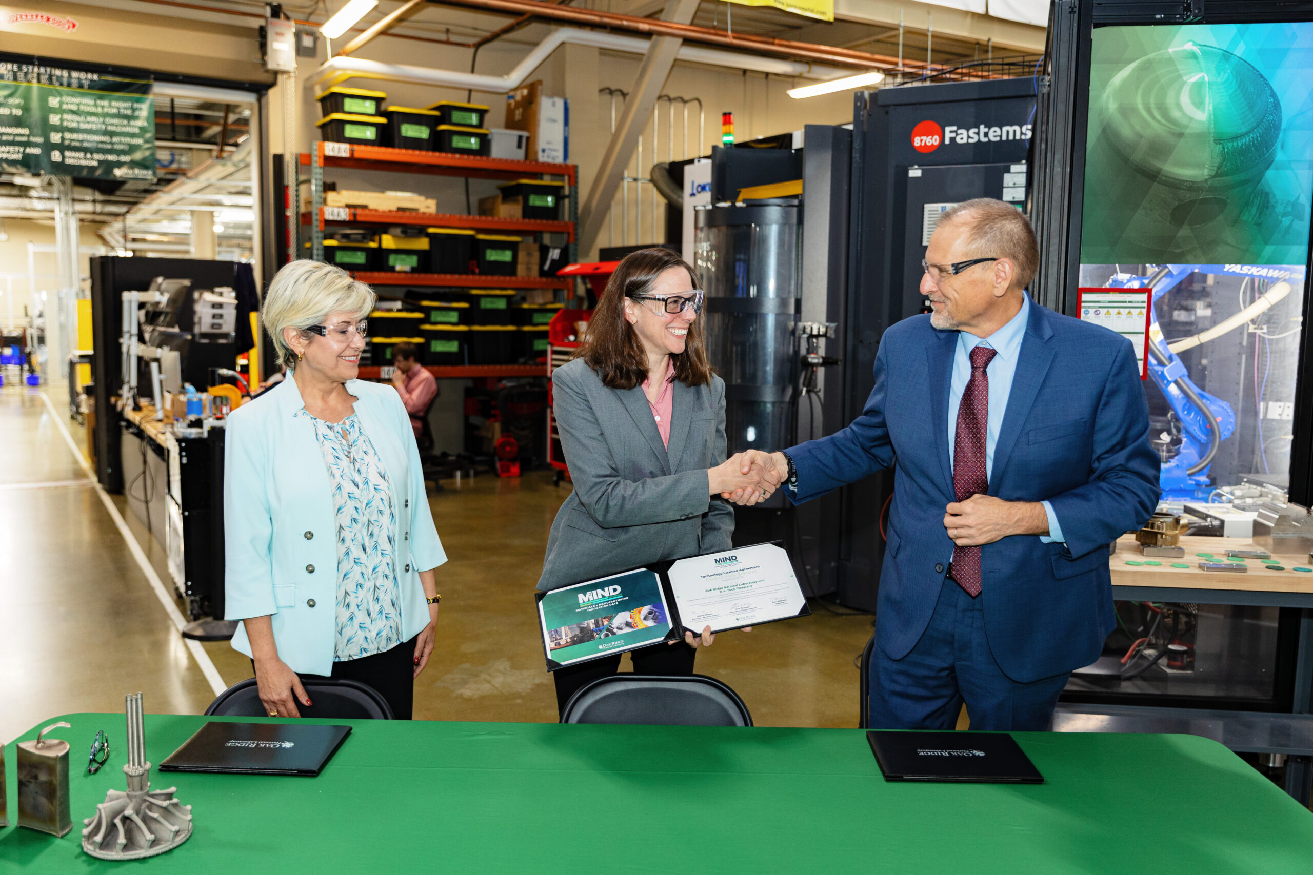 Two people shake hands during an agreement signing in a manufacturing facility.