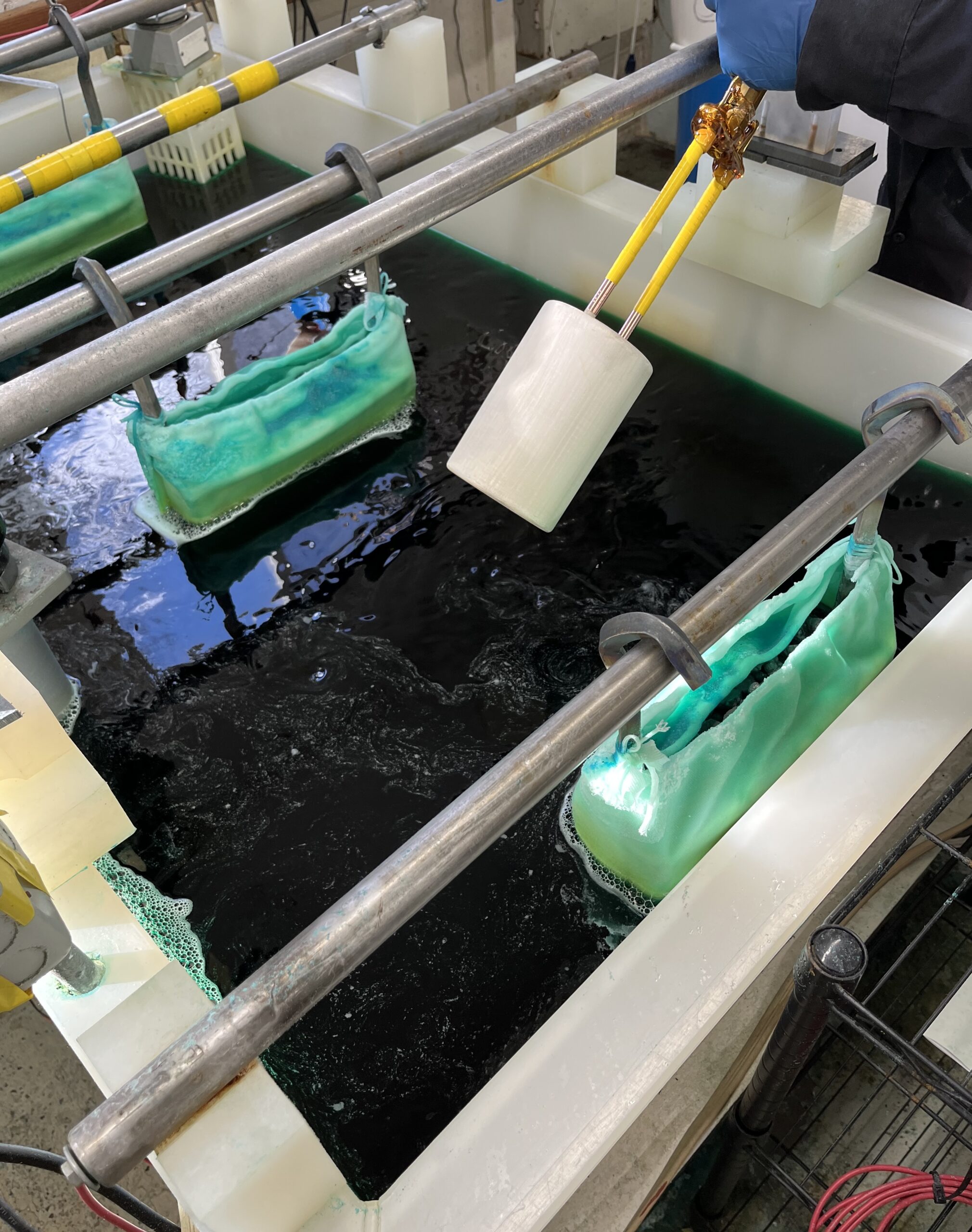 Gloved hand holding a white sample above a liquid-filled laboratory tank.