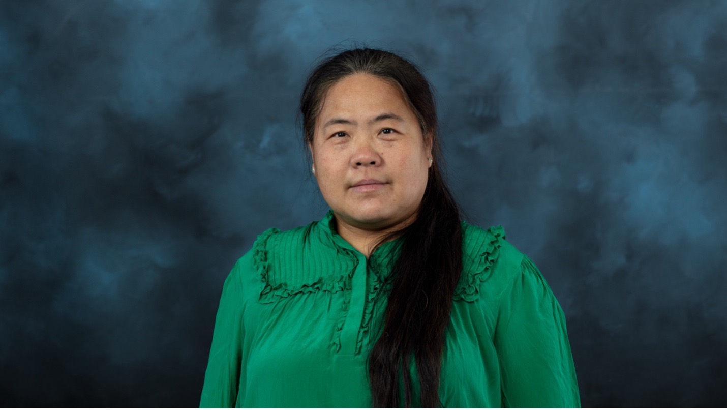 Woman in a green blouse posing against a blue-gray studio backdrop.