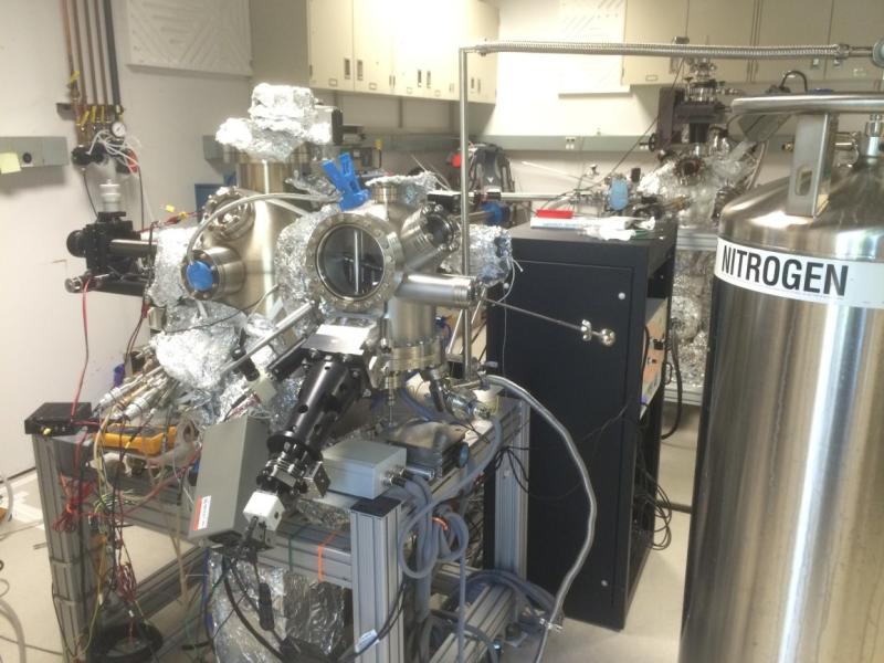 A complex metallic instrument next to a large cylindrical tank