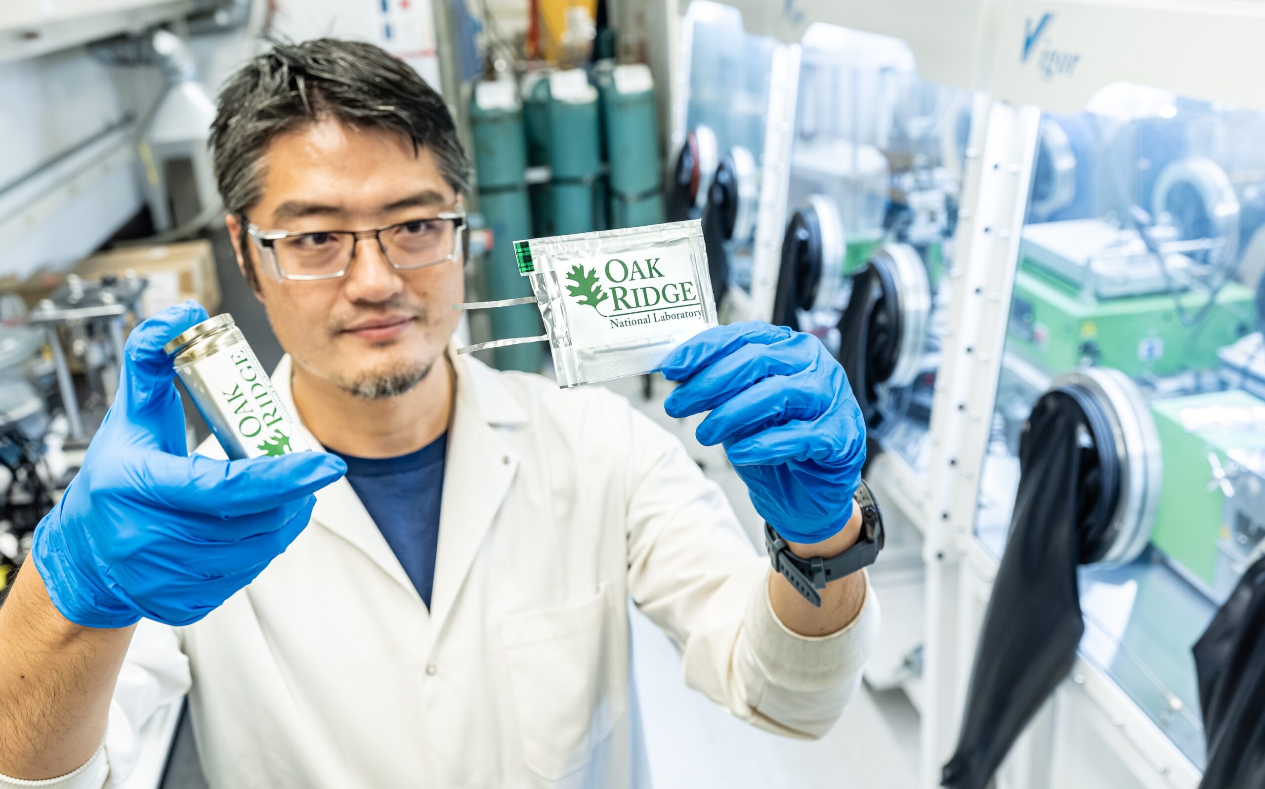 ORNL researcher holds two battery prototypes in a laboratory.