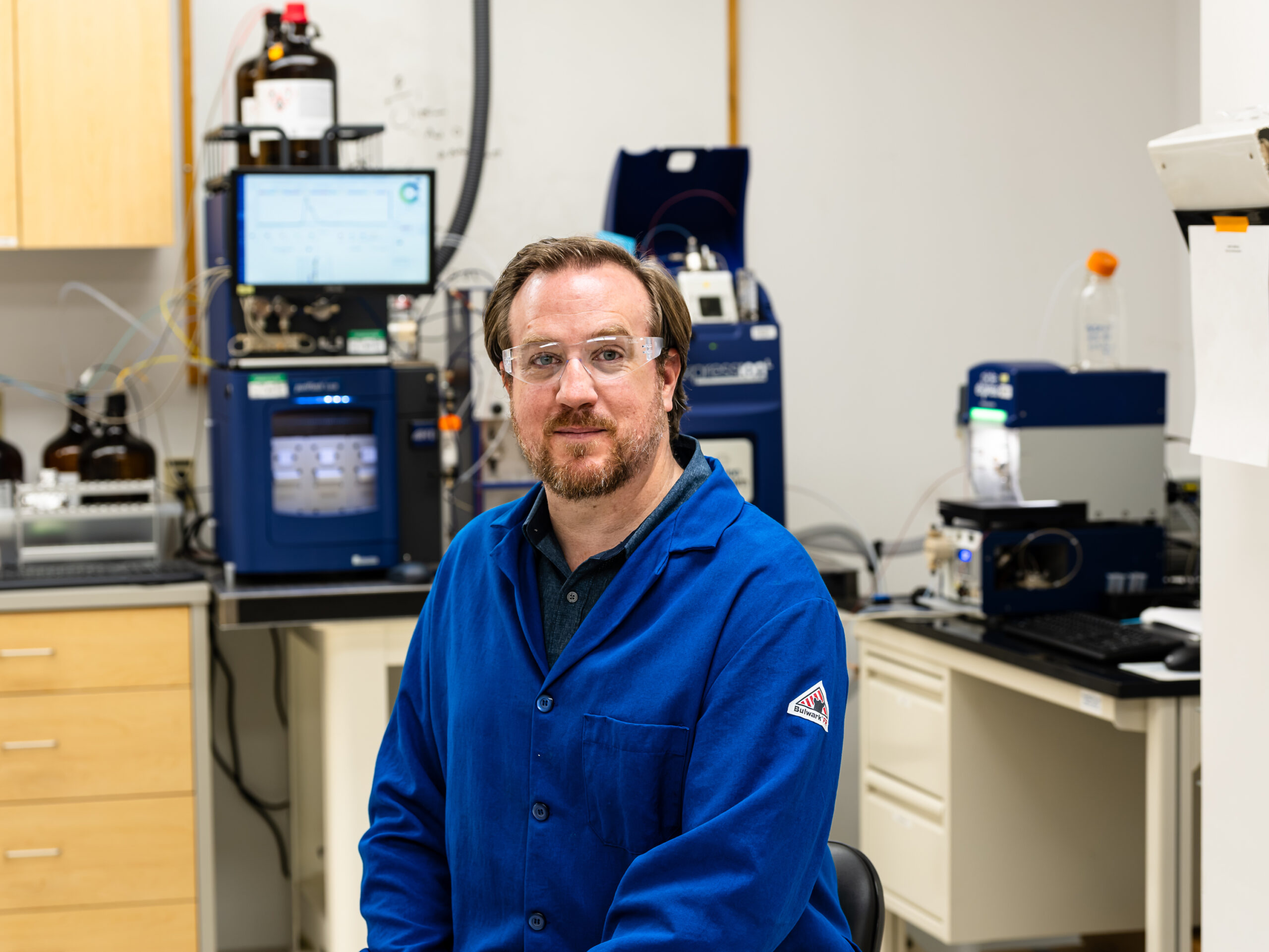 Researcher stands beside analytical equipment in a laboratory.