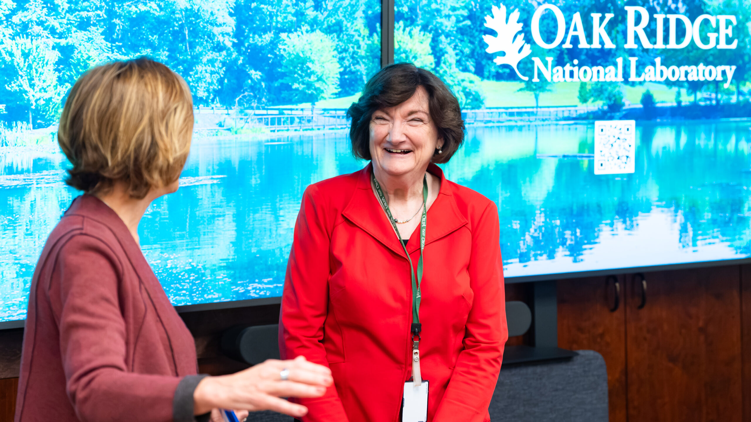 Two women talk in front of a monitor. 