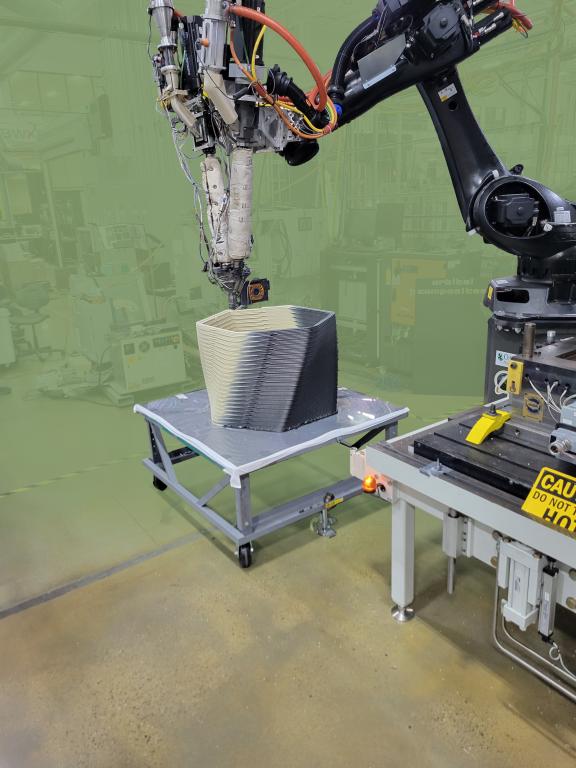 Robotic arm additively manufactures a layered concrete structure.