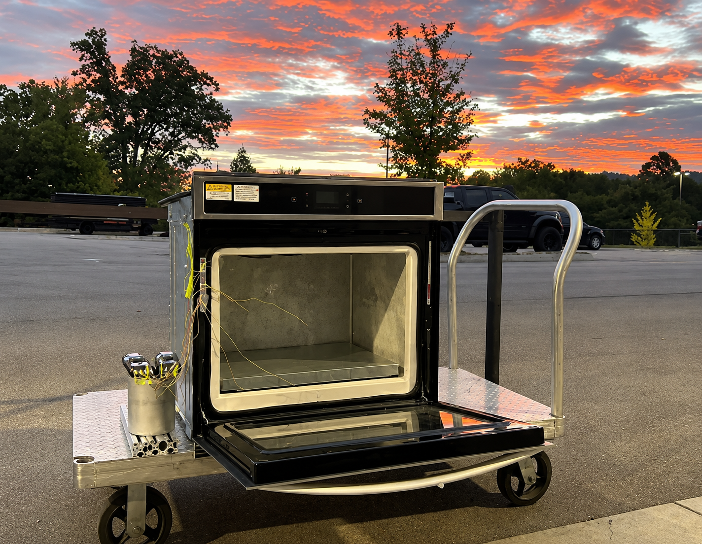 Instrumented oven sits on a cart outdoors at sunset.